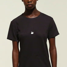 Load image into Gallery viewer, A model wearing a black short-sleeve crewneck t-shirt with a small white rabbit logo on the left chest, set against a plain light beige background.